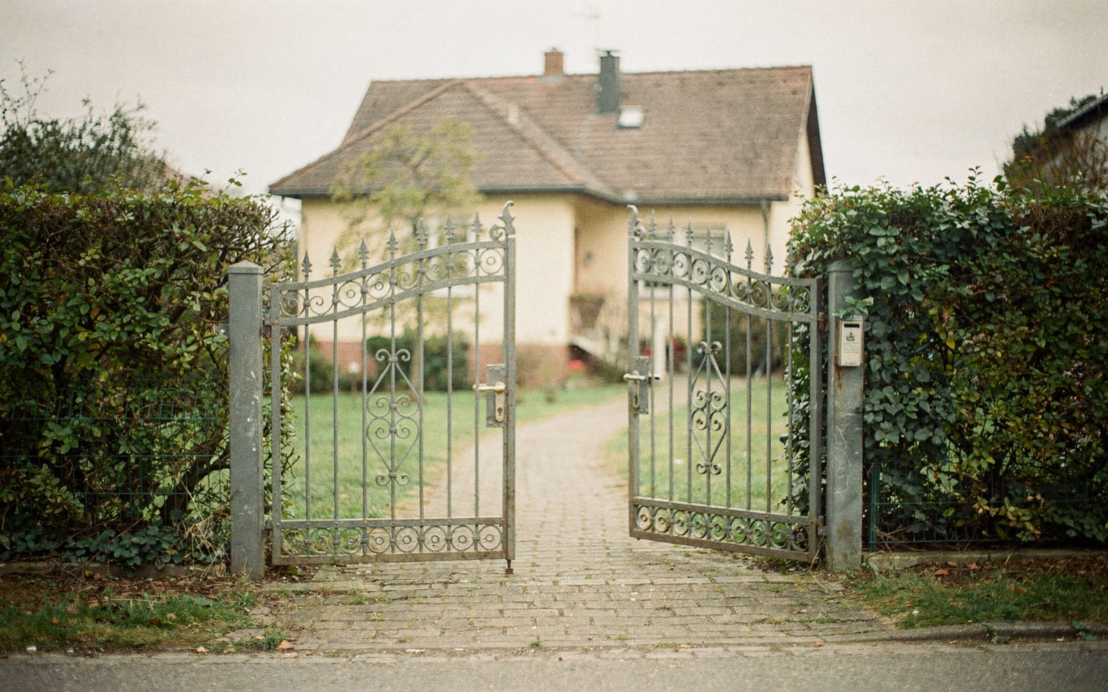 Halb geöffnetes schmiedeeisernes Gartentor an einem gepflasterten Weg zum Haus, Symbolbild zum Ratgeber über haus schnell verkaufen